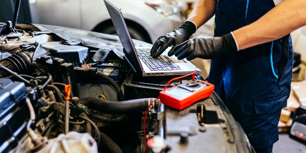 Car mechanic at work. Car an electrician using computer in auto repair shop. Close up.