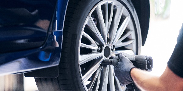 Mechanic changing car wheel in auto service using pneumatic wrench